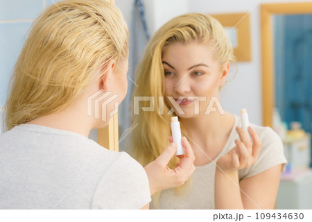 Woman in bathroom applying lip balm Woman in bathroom applying lip balm 109434630