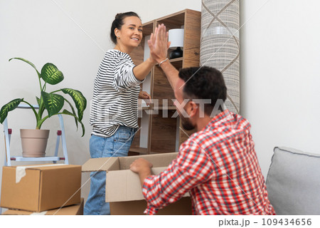 Positive man and woman highfive each other after successfully completing unpacking cardboard boxes with things in new apartment of residential complex friendly gesture and joy Positive man and woman highfive each other after successfully completing unpacking cardboard boxes with things in new apartment of residential complex friendly gesture and joy 109434656