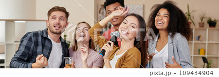 Party fun. Young asian girl holding microphone and singing while playing karaoke with best friends at home. Group of people drinking, having fun together Party fun. Young asian girl holding microphone and singing while playing karaoke with best friends at home. Group of people drinking, having fun together 109434904
