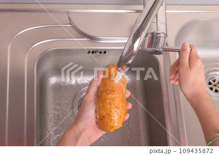 Female hands washing potato with hand under running water in sink in the kitchen 109435872