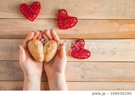 Heart shaped potatoes in hands on a wooden background. Valentine's day concept. Ugly vegetables. 109436390