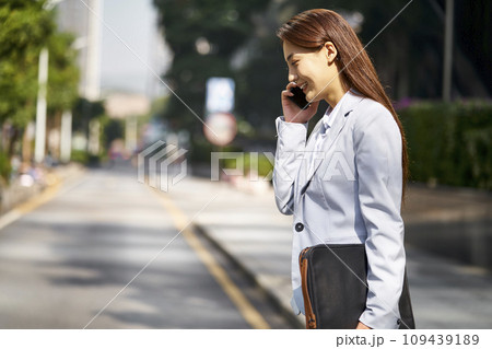 young asian white collar office lady talking on cellphone while walking in street 109439189