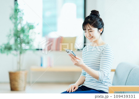 リビングでスマホを操作する若い女性。 109439331