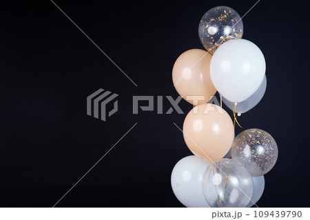 On a black background, balloons of light shades - white, beige, transparent - are flying. Space for text 109439790