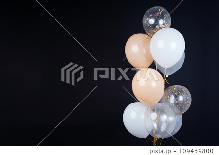A bunch of balloons in white, beige and transparent colors on a dark background with space for an inscription 109439800