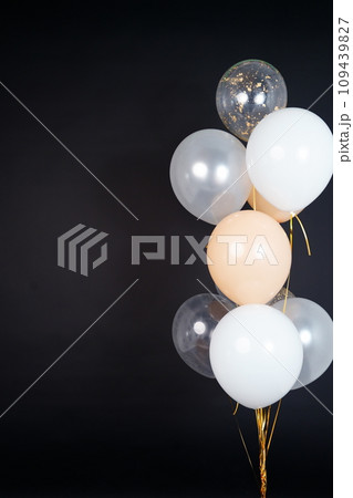 On a black background, balloons of light shades - white, beige, transparent - are flying. Space for text 109439827