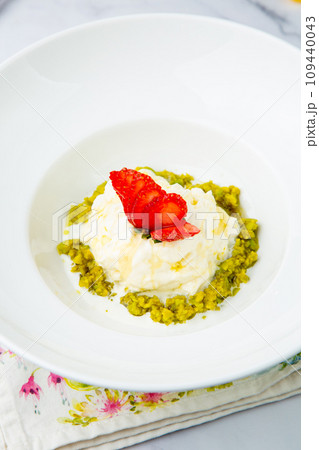 curd dessert with strawberries on top in a white plate on a marble background, side view 109440043