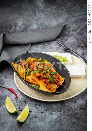 nachos with sauce, meat and herbs in a black plate, side view 109440314
