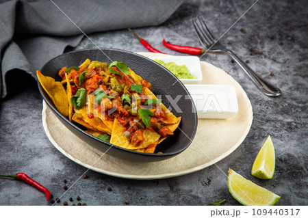 nachos with sauce, meat and herbs in a black plate, side view 109440317