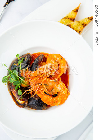 shrimp and mussels with herbs in a white plate with toasted bread, side view 109440560