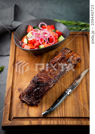 well-done steak with tomato and cucumber salad on a wooden tray, side view 109440725