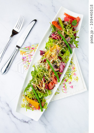 green salad with cherry tomatoes on a white oblong plate, side view 109440818