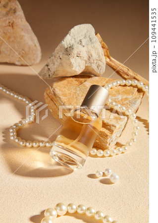 On a beige background with stone and pearl necklace, a glass perfume bottle unlabeled displayed. Minimal concept for advertising with mockup for design 109441535