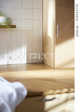 A sunny kitchen with white tile walls, a wooden table and sink. 109443743