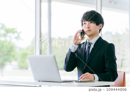 スマートフォンで話しながらパソコンを使う若いアジア人ビジネスマン 109444806