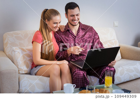 Cute young couple having breakfast, in front of laptop computer Cute young couple having breakfast, in front of laptop computer 109449309