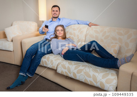 Portrait of happy couple sitting on sofa watching television together Portrait of happy couple sitting on sofa watching television together 109449335