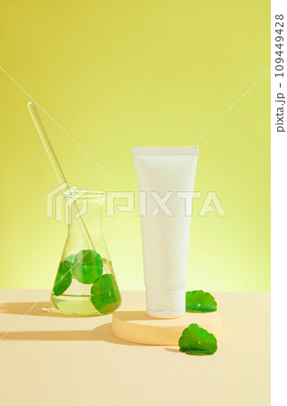 White mockup bottle for branding with gotu kola leaves decorated on round podium and glass flask on green background. Space for presentation cosmetic of centella extract, front view White mockup bottle for branding with gotu kola leaves decorated on round podium and glass flask on green background. Space for presentation cosmetic of centella extract, front view 109449428