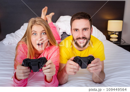 Happy young couple having fun playing videogames in bed Happy young couple having fun playing videogames in bed 109449564
