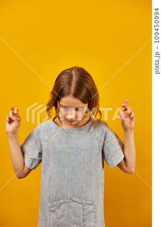 Teen girl fingers crossed on yellow studio background Teen girl fingers crossed on yellow studio background 109450994