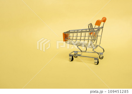 Small cart on a yellow background. Small supermarket grocery push cart for shopping. Shopaholic. Buyer. Shopping concept. Close-up. Isolated shopping trolley on a yellow background. Copy space. 109451285