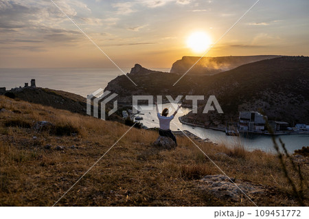 Happy woman on sunset in mountains. Woman siting with her back on the sunset in nature in summer with open hands. Silhouette. 109451772