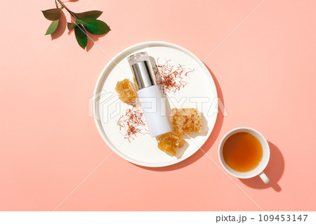 Empty label bottle decorated with saffrons and beeswax on a dish. Green leaves and a cup of tea featured. Blank label for branding mock-up 109453147
