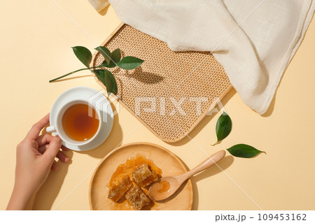 Round wooden dish featured cubes of beeswax. Hand model holding a teacup. Bamboo tray with blank space for product promotion 109453162