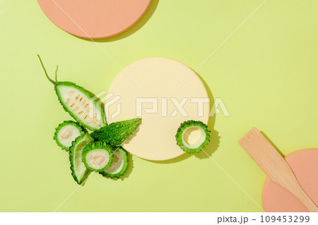 On a green background with color podiums, fresh bitter melon slices decorated. Blank space for display product. Vitamin E in the bitter gourd mask helps to hydrate and soften the skin 109453299