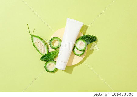 An unbranded plastic tube decorated with bitter melon slices on green background. Mockup for design, organic cosmetics, beauty products concept. Bitter gourd is an effective dermatological treatment 109453300