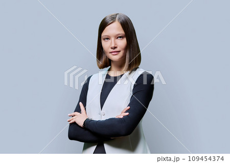 Young confident woman with crossed arms looking at camera on gray background Young confident woman with crossed arms looking at camera on gray background 109454374
