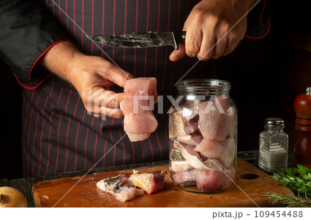 The chef prepares fresh carp fish. The cook's hand puts a fish steak into a jar for pickling. Working environment in a restaurant kitchen 109454488
