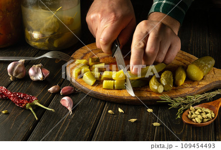 The process of preparing a delicious dish with pickles for lunch. The chef cuts a pickled cucumber into small pieces with a knife. Work environment on kitchen table with spices and seasonings 109454493