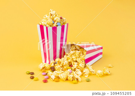 Two striped carton buckets with caramel popcorn and dragee candies on yellow background 109455205
