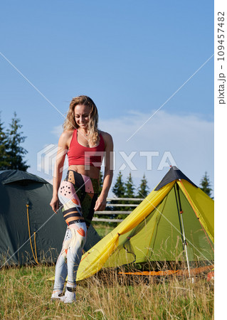 Woman hiker camping in mountains. Woman wearing sportswear, traveling, hiking outdoors. Pretty, young female posing, smiling, having break. Concept of harmony with nature. 109457482