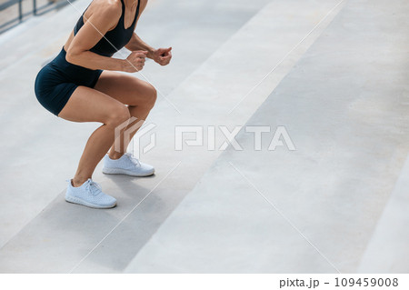 Woman in black sports shorts doing squats on the stairs 109459008