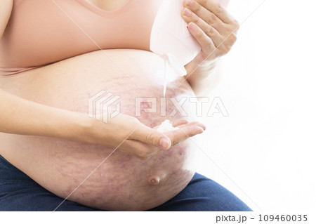 妊娠線ができたお腹にクリームを塗る女性の手と臨月のお腹 109460035