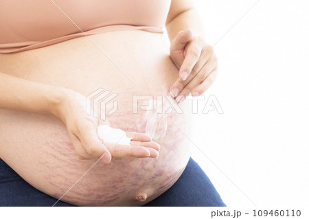 妊娠線ができたお腹にクリームを塗る女性の手と臨月のお腹 109460110