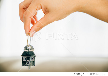 Hand holds house key marking homeowners' achievement. Agent presents model home symbolizing real estate success. Confidence and happiness shine. Hand holds house key marking homeowners' achievement. Agent presents model home symbolizing real estate success. Confidence and happiness shine. 109460660