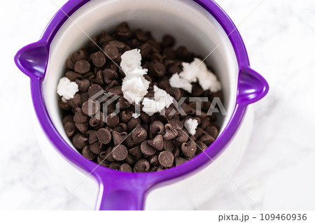 Melting chocolate chips in a candy melting pot to make chocolate icing for panda-shaped shortbread cookies. 109460936