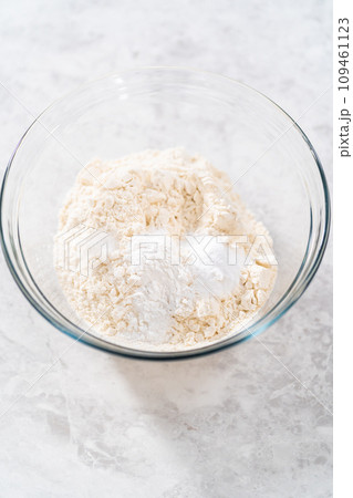 Mixing dry ingredients with a hand whisk in a large glass mixing bowl to bake banana cookies with chocolate drizzle. 109461123