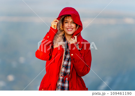 Close up beautiful Caucasian woman stand near cliff with hold coat hood and stay on the mountain with warm light of sun rise and she look happiness with smiling also look at camera. 109461190