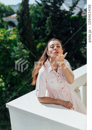 Beautiful woman in summer light dress on balcony looking at the street Beautiful woman in summer light dress on balcony looking at the street 109463496