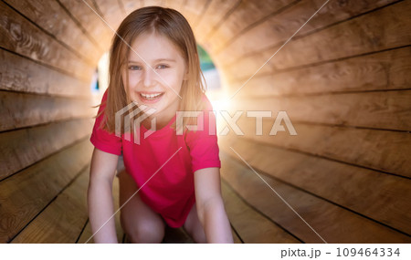Smiling little girl sitting in wooden pipe in park Smiling little girl sitting in wooden pipe in park 109464334