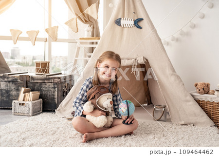 Little girl with teddy bear and globe sitting in wigwam settled in playroom 109464462