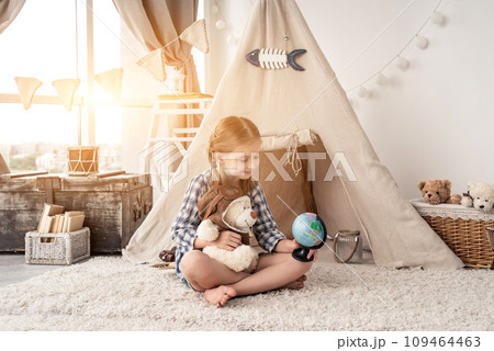 Little girl exploring globe with teddy bear sitting in wigwam in playroom Little girl exploring globe with teddy bear sitting in wigwam in playroom 109464463