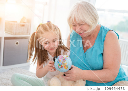 Happy granny showing globe to interested granddaughter in light room 109464478