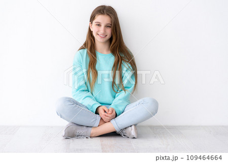Pretty teenage girl sitting on floor leaning against white wall 109464664