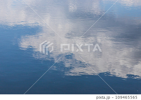 Calm water surface. Summer evening near a forest lake, the surface of the water is smooth, with small waves. The sky with clouds is reflected from the surface, coloring the water in different colors 109465565