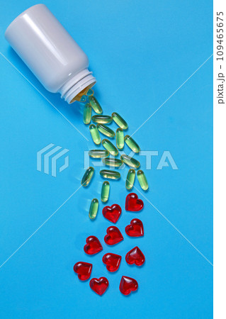 Omega-3 polyunsaturated fatty acids and red hearts pour out from a white plastic jar on a blue background. Prevention and treatment of atherosclerosis 109465675